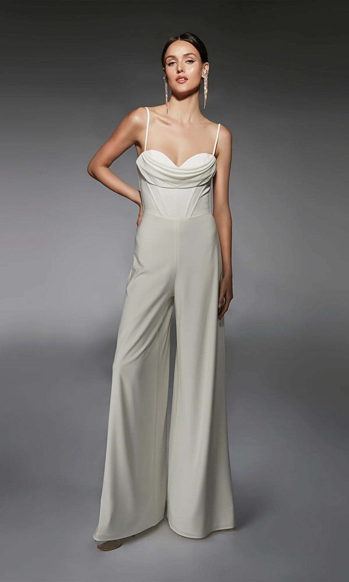 A woman poses with one hand on her hip in the Alyce 70075 Long Formal Jumpsuit, featuring a sleeveless design, corset-boned bodice, and wide-leg pants in Diamond White against a neutral background.